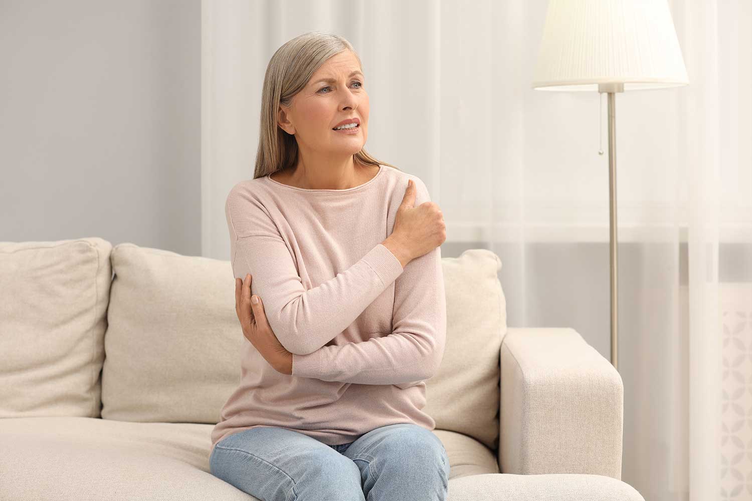 eine Frau sitzt auf einer Couch und hält ihre Schulter