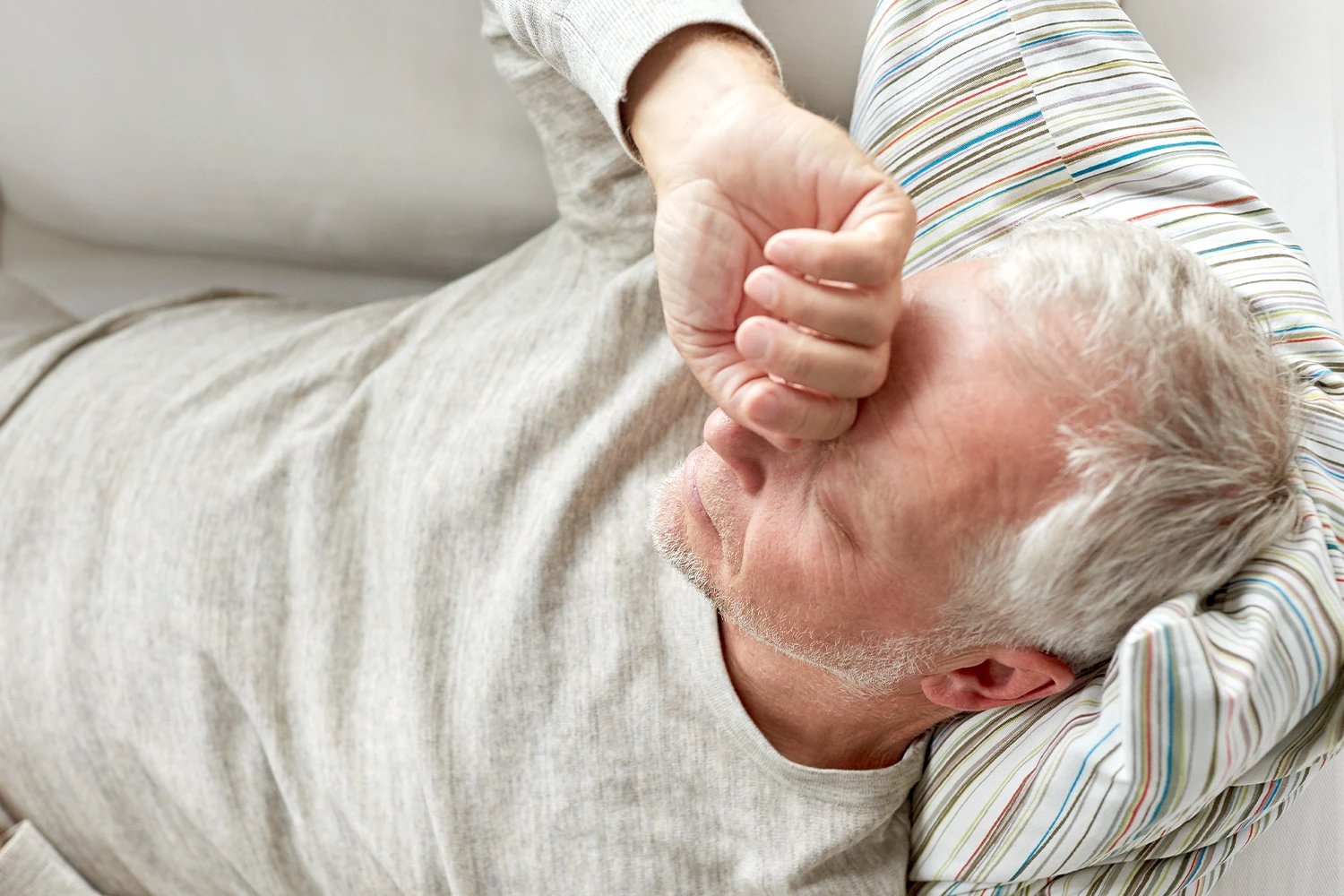 Älterer Mann liegt erschöpft auf dem Sofa, leidet unter Schlafstörungen.